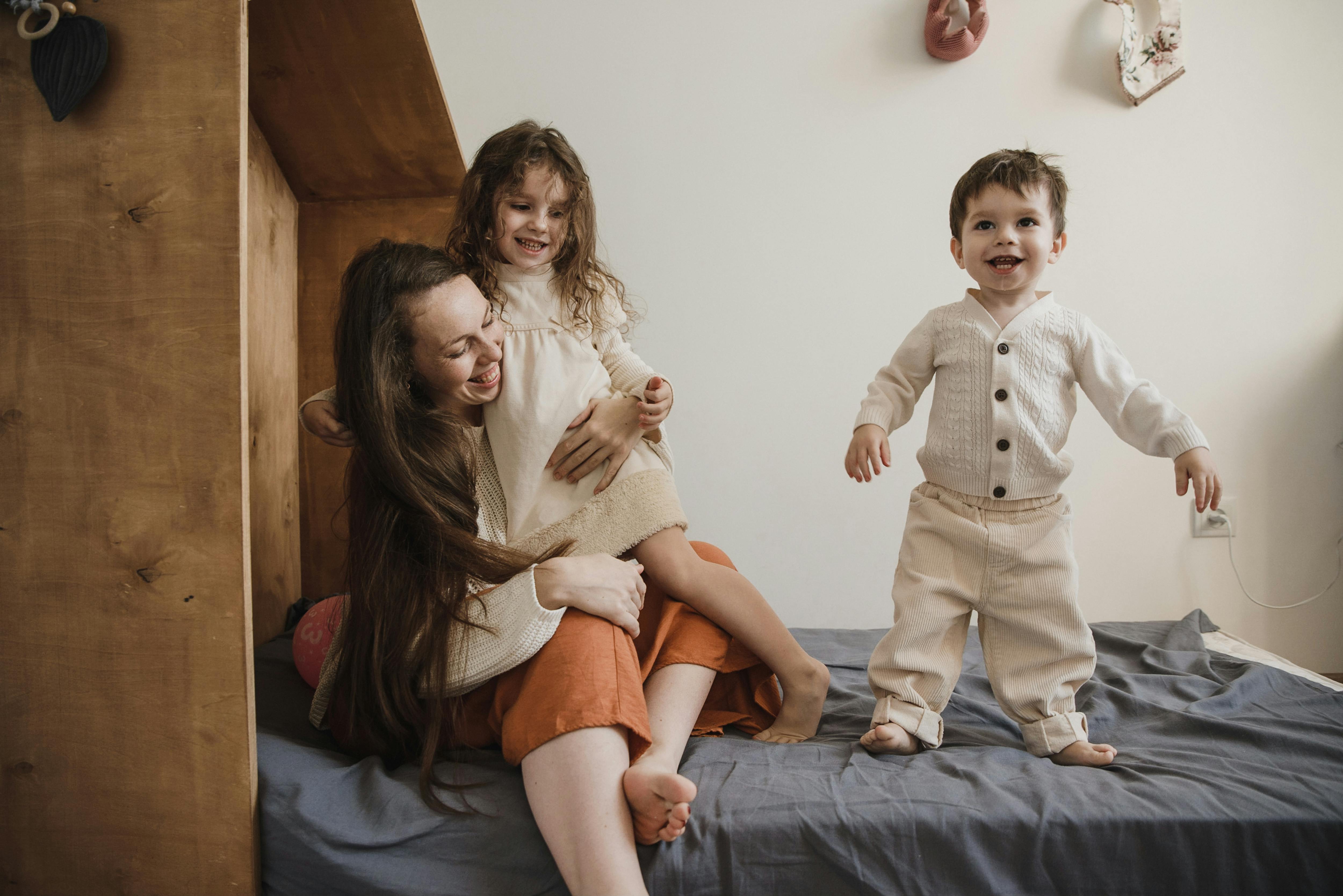 woman playing with children on bed