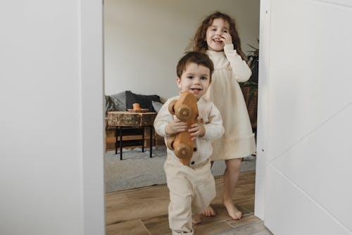 Little Girl and Boy Standing Near White Door