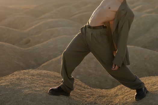 一名赤裸上身的男子穿着西装，在沙质沙漠地形上动态地摆出姿势