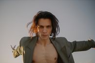 一名年轻人穿着时尚夹克和敞开衬衫，自信地在户外摆着姿势，戏剧性的灯光让场景更具张力