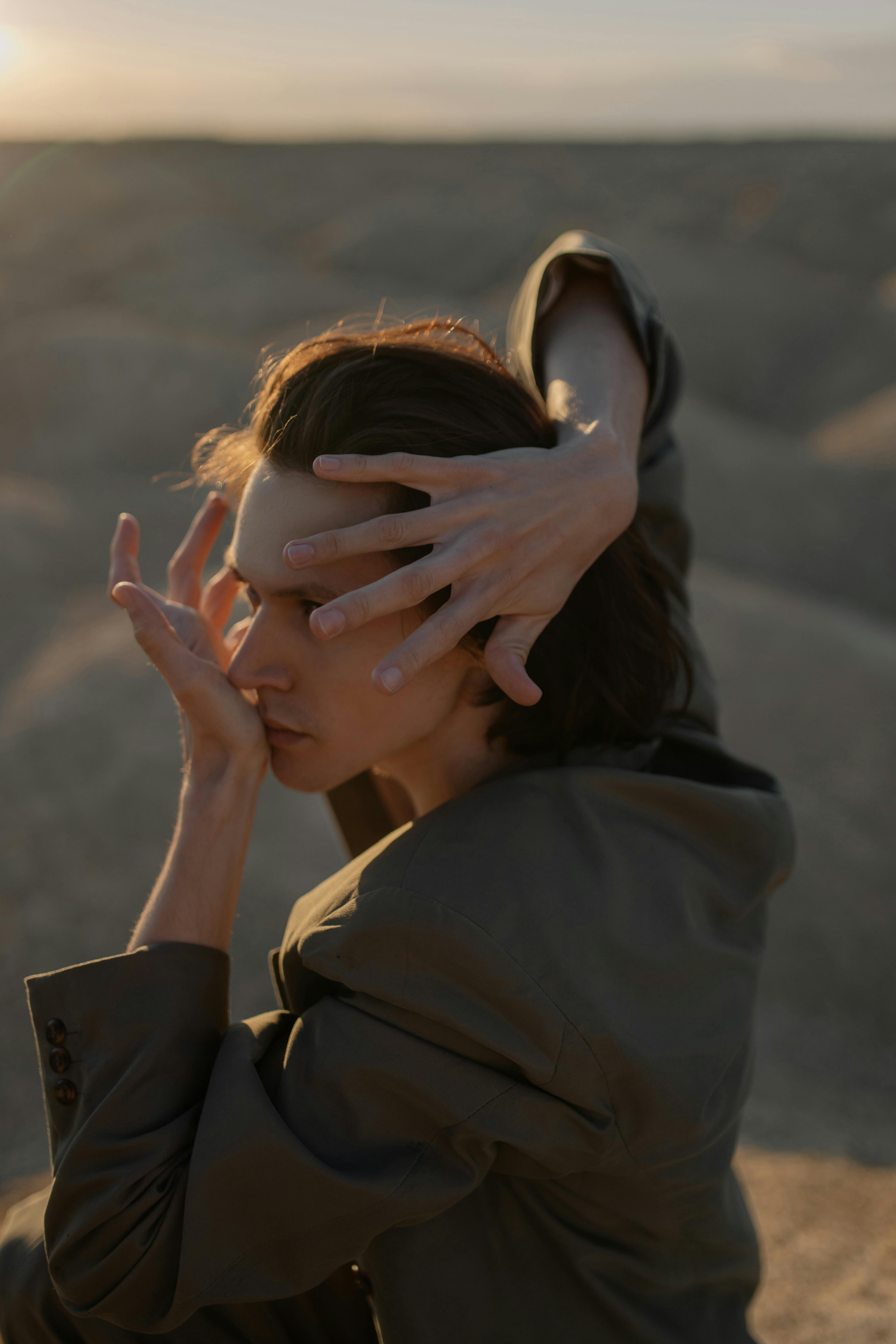 Evocative portrait capturing a man posing with hands in a desert landscape, showcasing fashion and emotion.