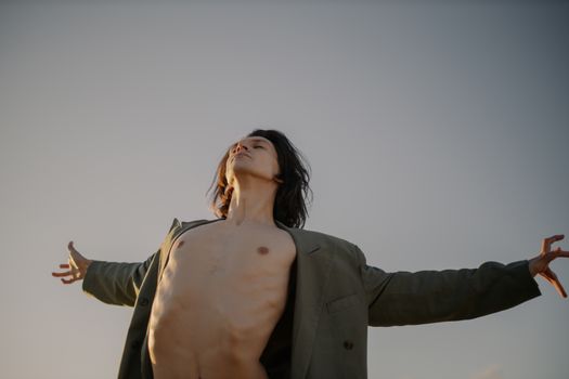 一个赤裸上身、敞开夹克的男人，在晴朗的天空下展现着大自然的自由