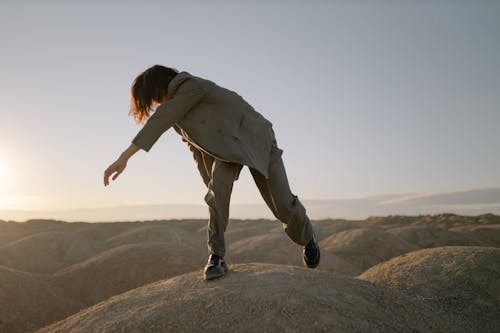 Woman in Gray Jacket and Brown Pants Jumping on Brown Rock