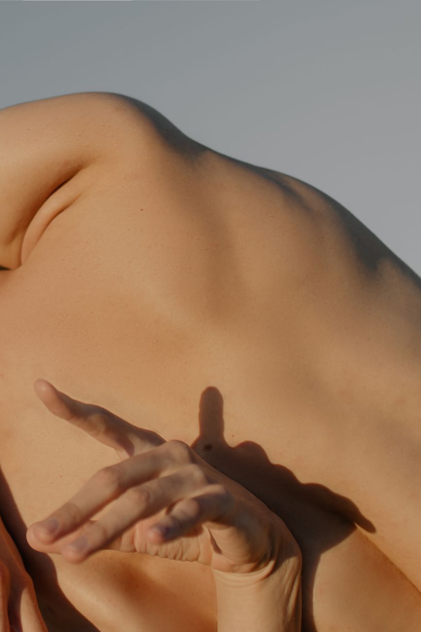 A close-up shot of a nude male back with graceful hand positioning, capturing form and detail.