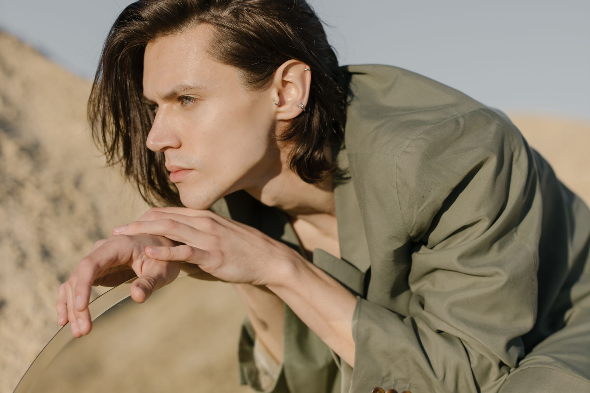 Stylish portrait of a man in a desert landscape holding a mirror. Modern fashion concept.