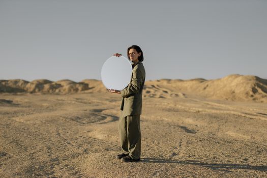 这幅艺术作品捕捉了一个男人在沙漠中手持圆镜的场景，象征着反思