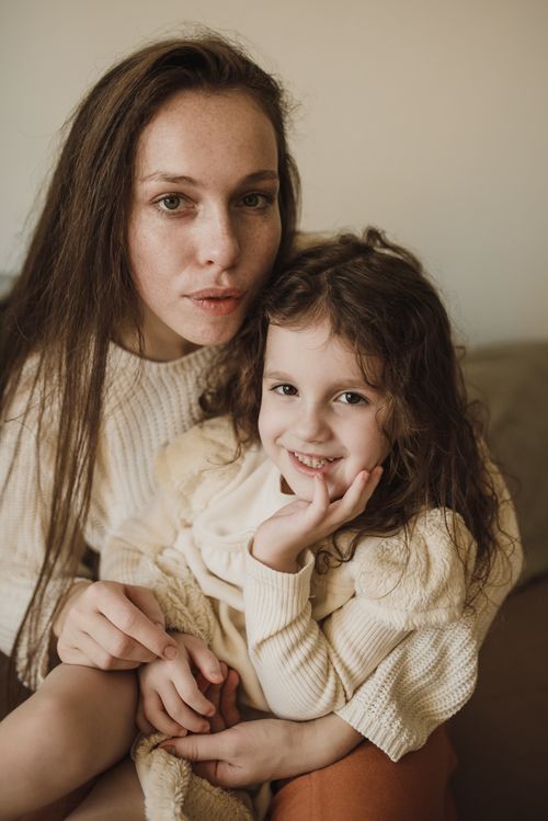 Free A warm, intimate portrait of a mother and daughter sitting together indoors, both smiling. Stock Photo