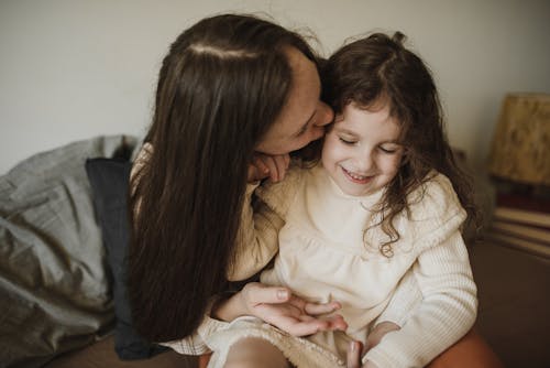 Mother Kissing Her Daughter while Sitting on Sofa