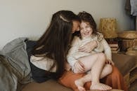 一位母亲坐在沙发上给女儿挠痒痒，母女俩欢笑嬉戏，共享温馨时光