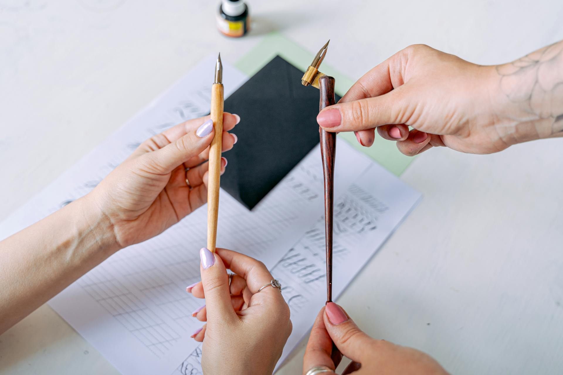 Close-up of hands holding calligraphy nib holders, emphasizing artistic focus.