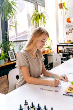 Young artist focused on drawing in a well-lit studio surrounded by plants and art materials.