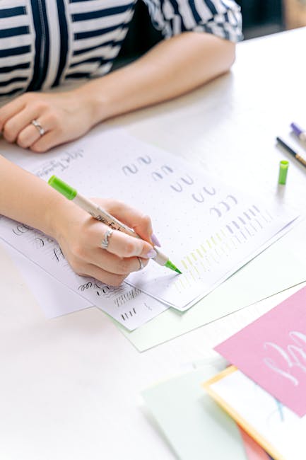 Close-up of a woman practicing hand lettering with a green marker on paper indoors.