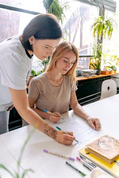 Instructor guides student in calligraphy workshop, focusing on hand lettering techniques.