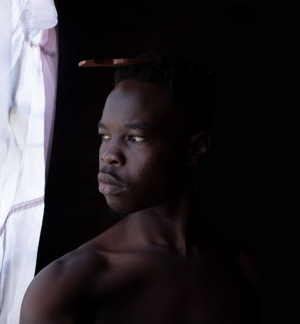 Intriguing portrait of a young man in low light, featuring dramatic shadows and a contemplative expression.
