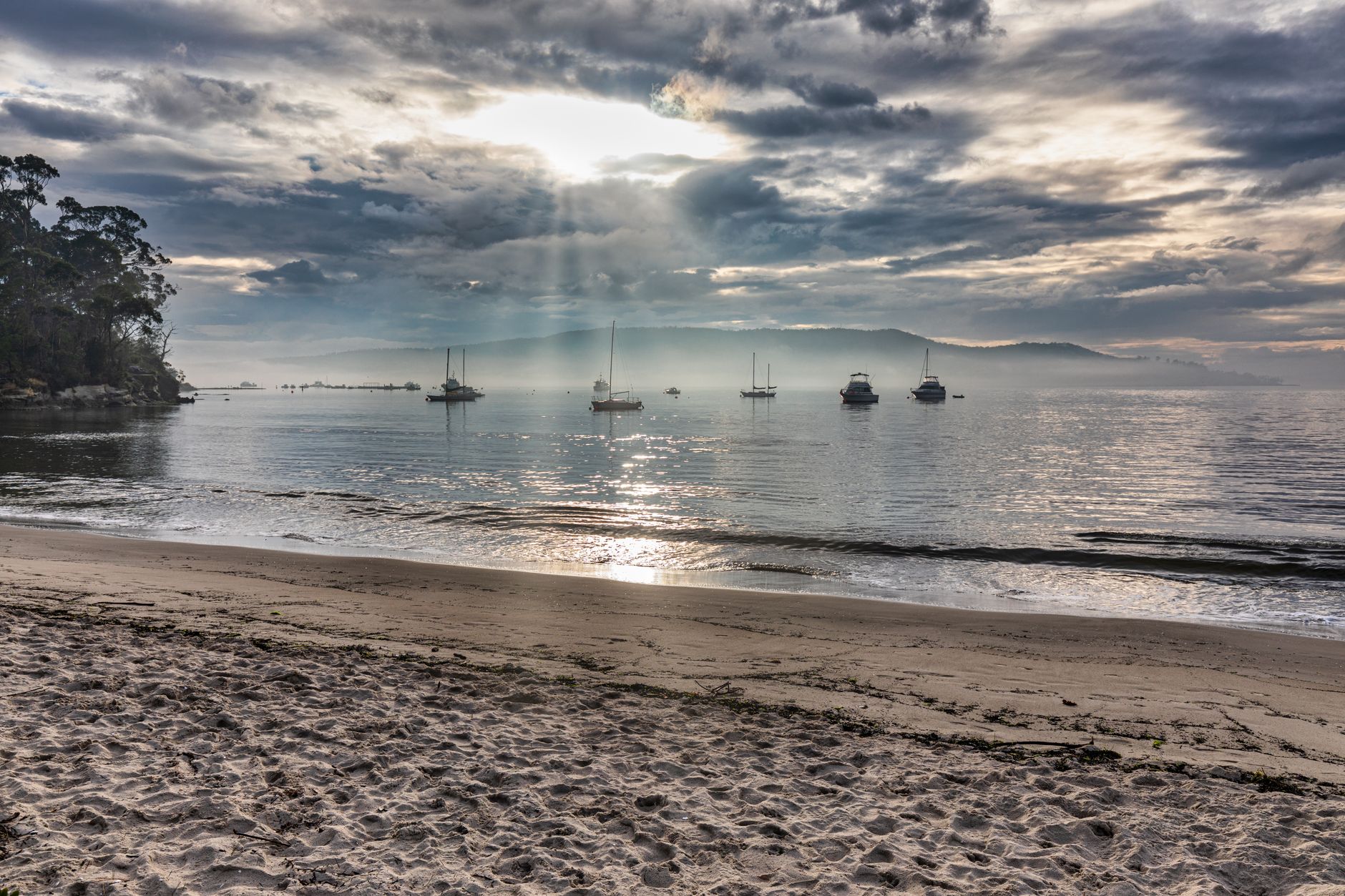 Tranquil sunrise over Snug Beach in Tasmania with boats on the calm water.