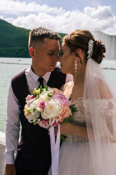 Intimate wedding moment with newlyweds by a lake in Russia, holding a vibrant bridal bouquet.