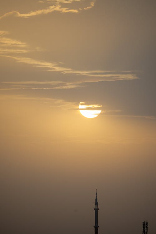 Picturesque view of bright yellow sun behind clouds in evening above tower of oriental building