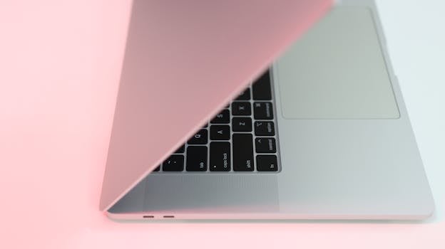 Modern laptop partially closed with a soft pink hue, perfect for tech-themed projects.
