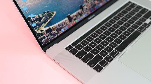 Free Close-up view of a sleek laptop with cityscape wallpaper on a pink background. Stock Photo
