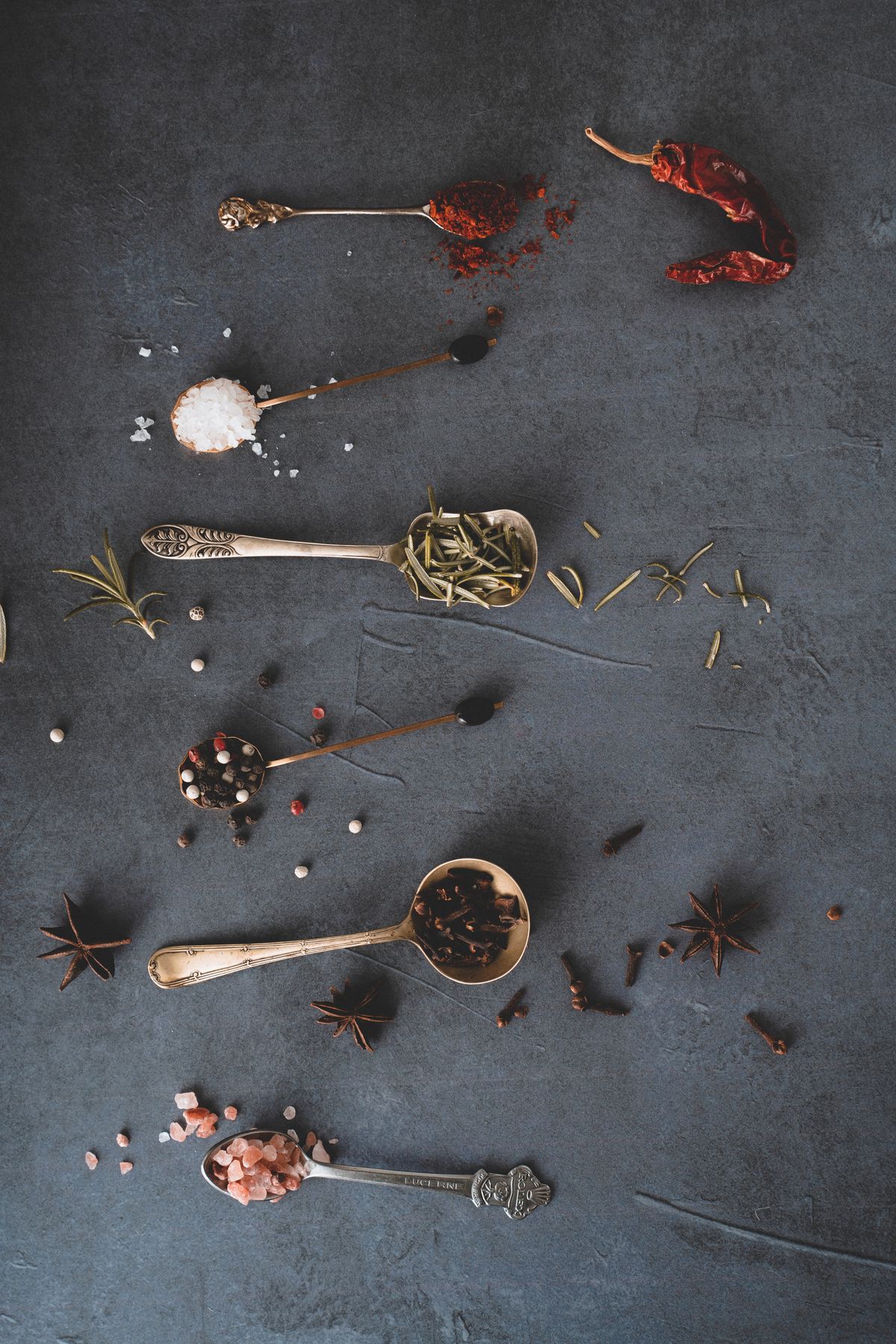Herbs and spices kept in separate spoons — rosemary, paprika, peppercorns and cloves