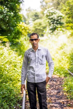 A man in sunglasses stands confidently on an overgrown railway track surrounded by lush greenery.
