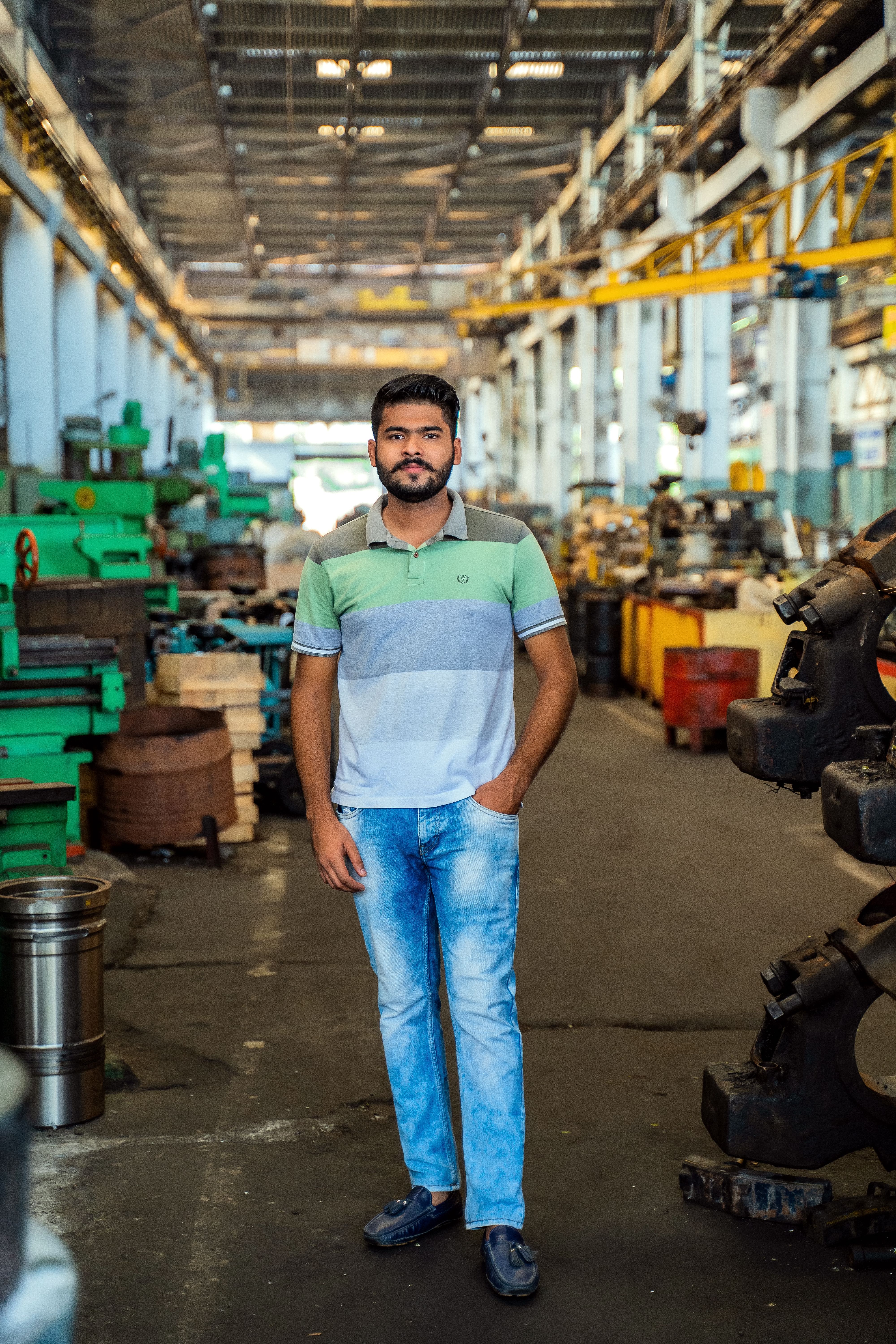 Bearded man in casual attire standing in a bustling industrial workshop.