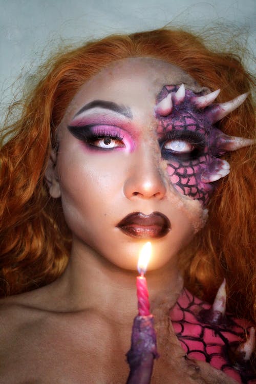 Person with unusual cool Halloween makeup holding glowing candle and looking at camera