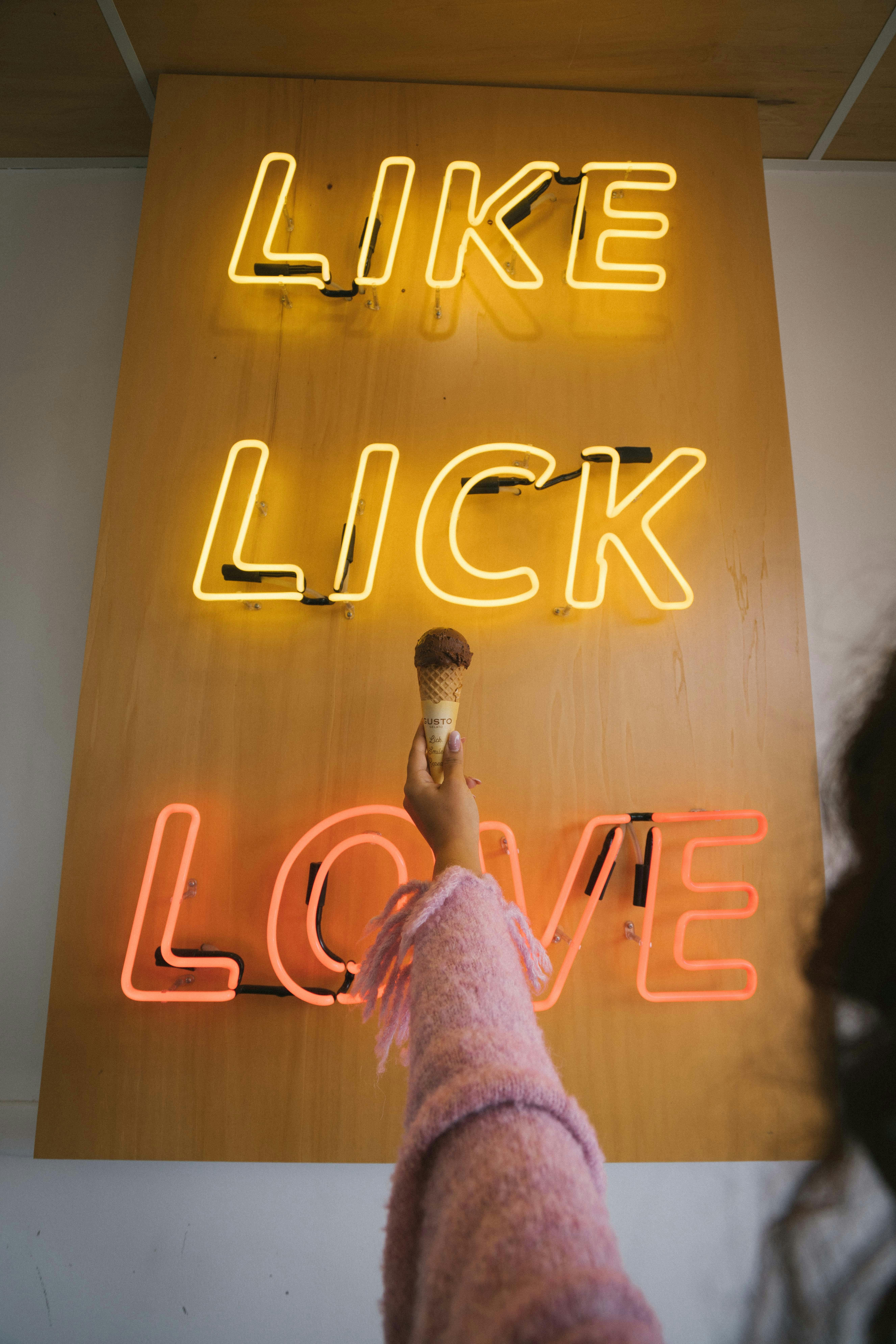 Hand holding ice cream cone under neon sign with text 'Like Lick Love' in Perth cafe.
