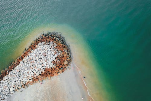 Drone view of calm turquoise ocean washing sandy shore with stones in daytime