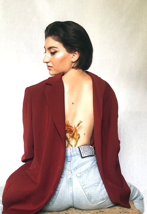 A Woman in Red Blazer and Denim Bottoms Sitting while Looking Over Shoulder