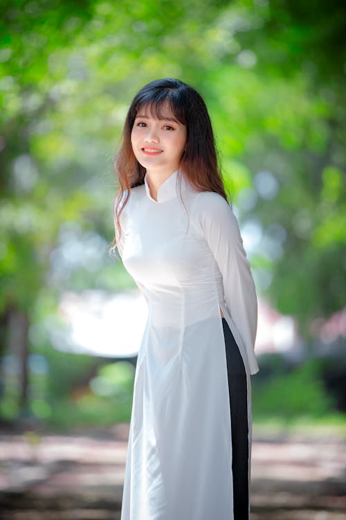 Cheerful Asian woman standing on street against green trees