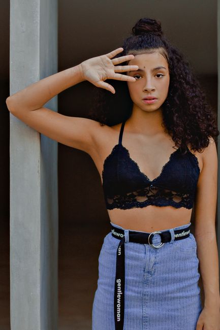 Young ethnic female in denim skirt with stylish belt leaning on glass and looking at camera