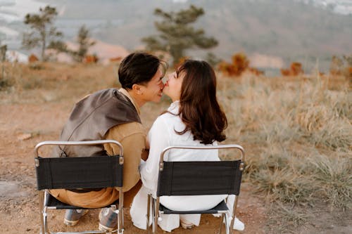 Back view of happy ethnic couple in love sitting on grassy hill and enjoying each other at daylight