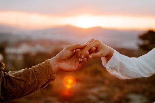 Free Crop faceless couple holding hands against picturesque mountains under colorful sky at sundown Stock Photo