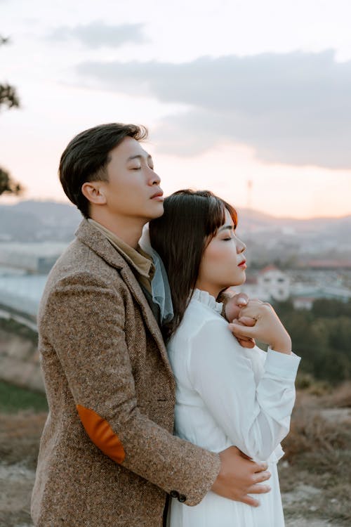 Side view of peaceful Asian newlywed couple embracing gently while spending romantic wedding day in nature together