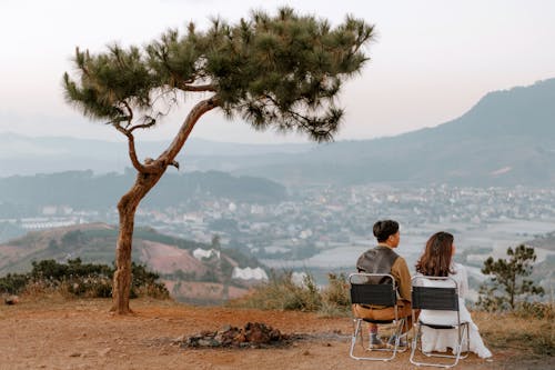 Back view full body of unrecognizable couple sitting on chairs close to each other and admiring view of city