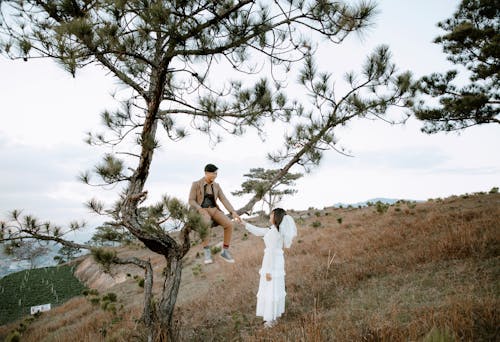 Full body of newly married couple holding hands and enjoying each other on grassy hill