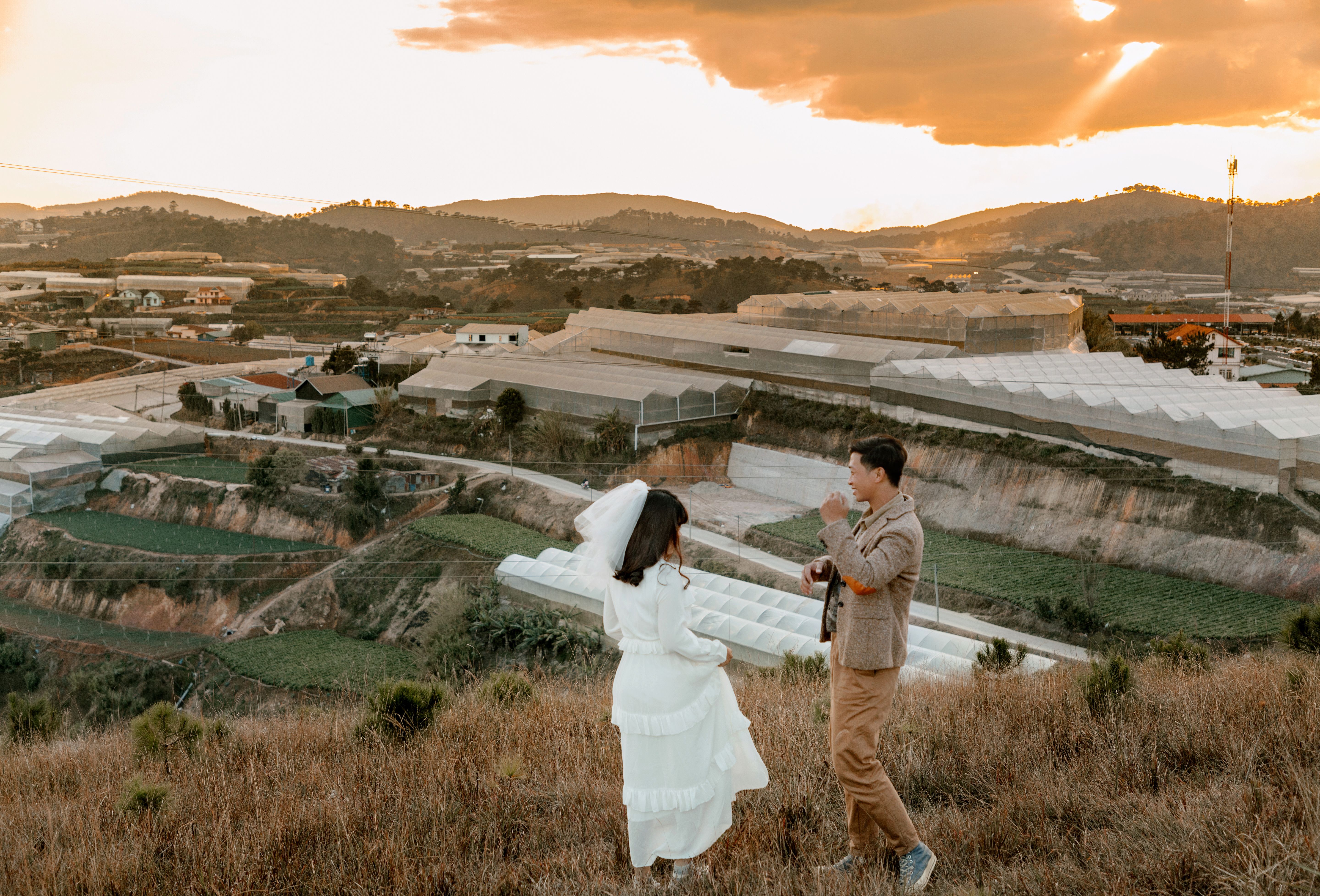 日落时分，一对年轻的新婚夫妇站在山上，从高角度拍摄的侧面图