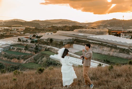 High angle side view full body of young newlywed couple standing on hill at sundown