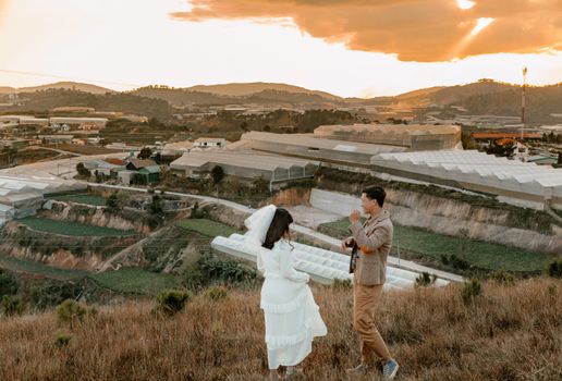 日落时分，一对年轻的新婚夫妇站在山上，从高角度拍摄的侧面图