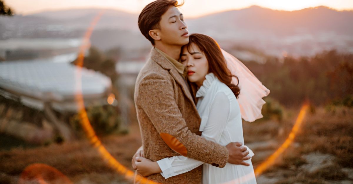 Side view of Asian newlywed couple hugging each other while spending wedding day together in nature