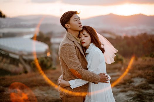 Side view of Asian newlywed couple hugging each other while spending wedding day together in nature
