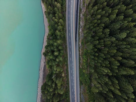 Aerial view showcasing a serene road bordered by lush forest and a turquoise lake in Whistler, BC.