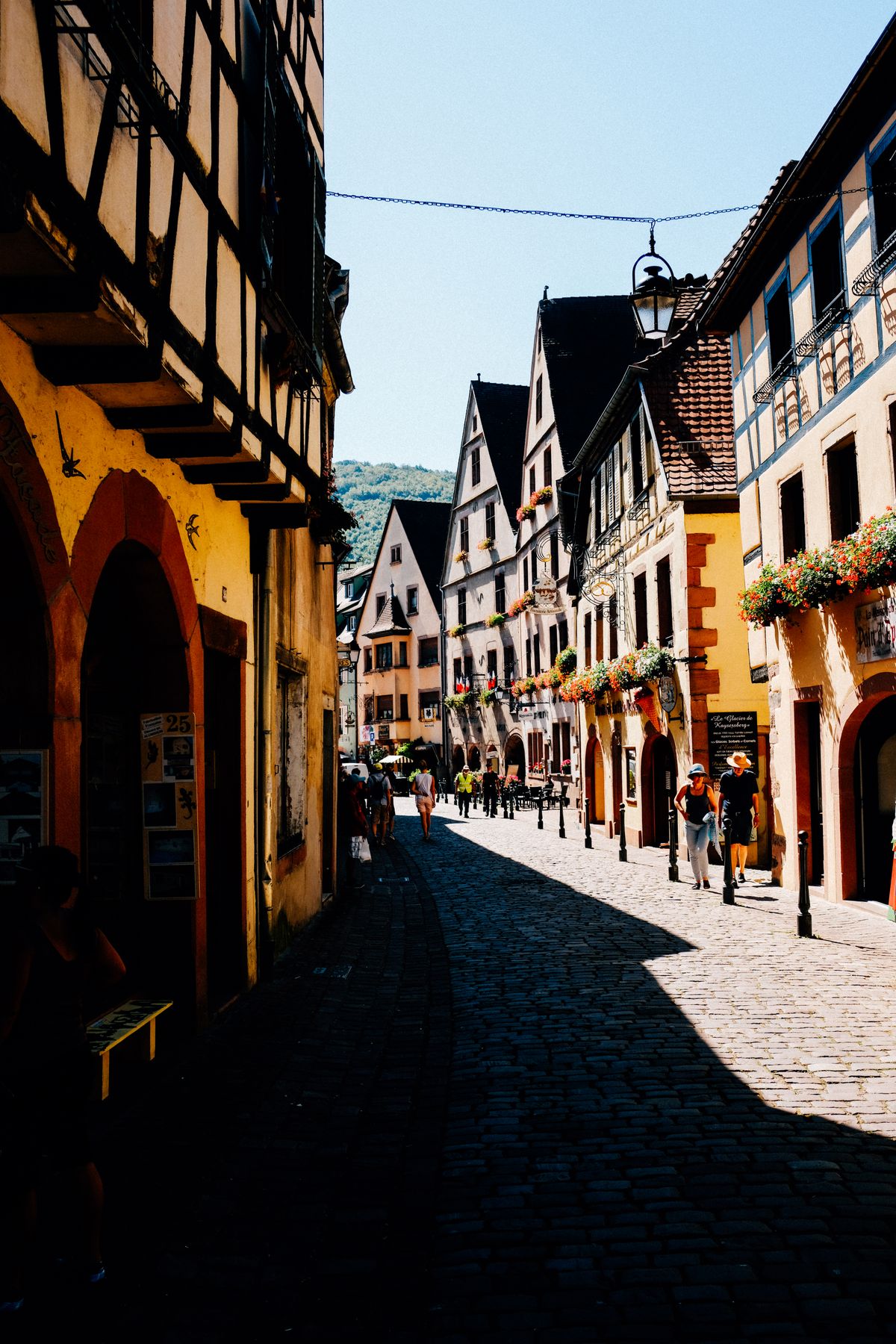 A sunlit cobblestone street between old timbered houses in a small European town.