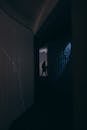 Silhouette of anonymous person walking in narrow concrete passage with neon lights on wall in darkness