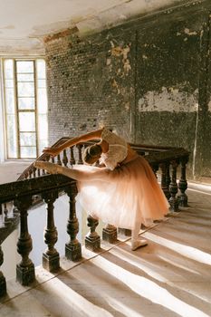Elegant ballerina stretching on rustic staircase with sunlight streaming through windows.