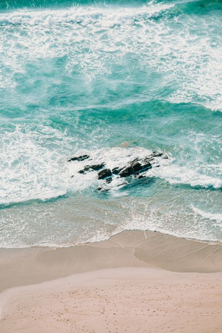 From above of foamy waves of turquoise ocean rolling on rocky coastline with sand in sunlight in tropical country in summer