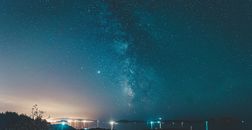 宁静水面附近的山地上空，夜空中星光点点，远处黑暗中灯光闪烁