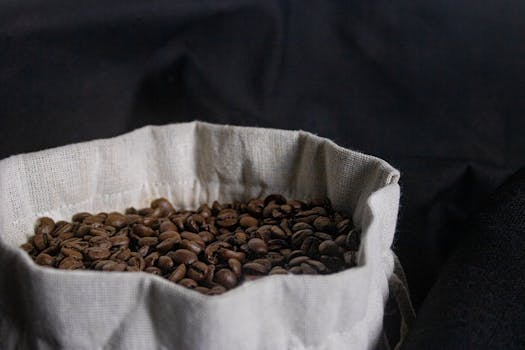 A close-up of aromatic roasted coffee beans in a rustic sack against a dark background.