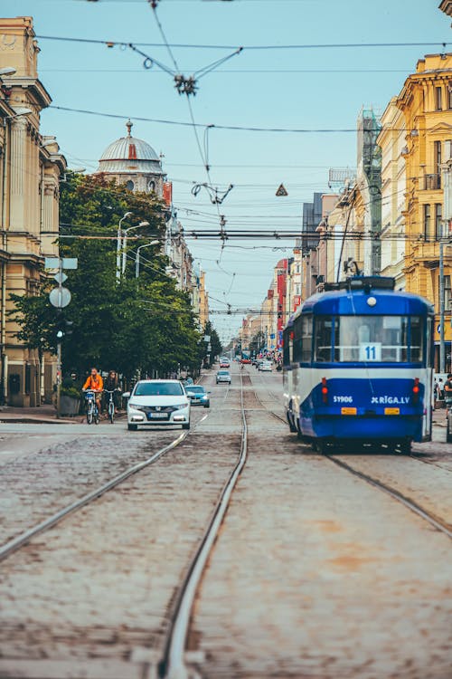 Modern tramway riding along paved city street near cars cyclists and old buildings in town